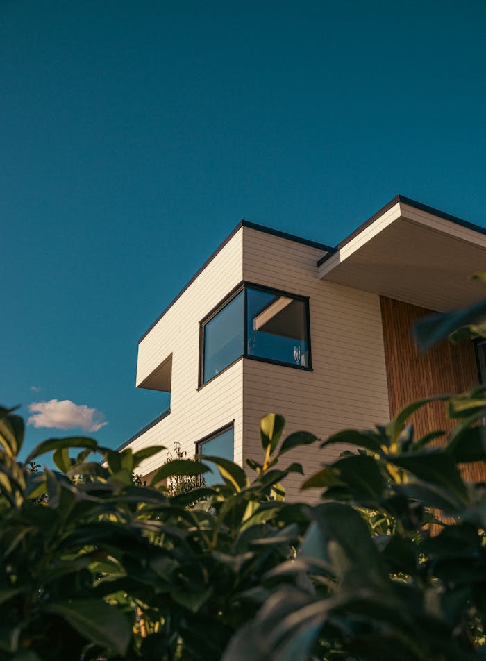 Elegant modern house with large windows and a clear sky background, framed by greenery.