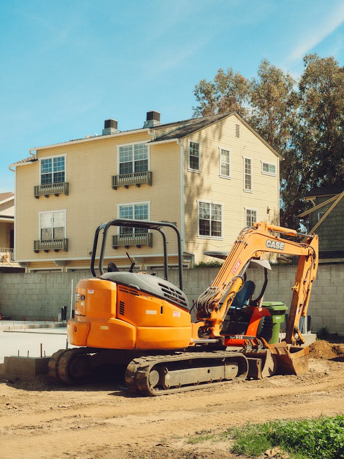 Yellow excavator at residential construction site in Los Angeles with homes in background.