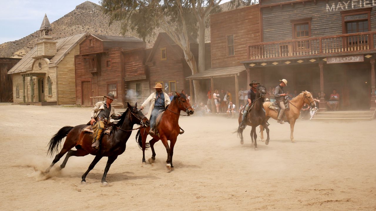 gallery-01 Cowboys on horseback perform reenactment in a Wild West town setting at Almería, Spain.