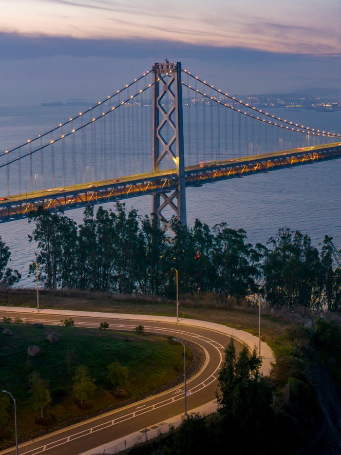 A stunning view of the illuminated San Francisco Bay Bridge at dusk over calm waters.