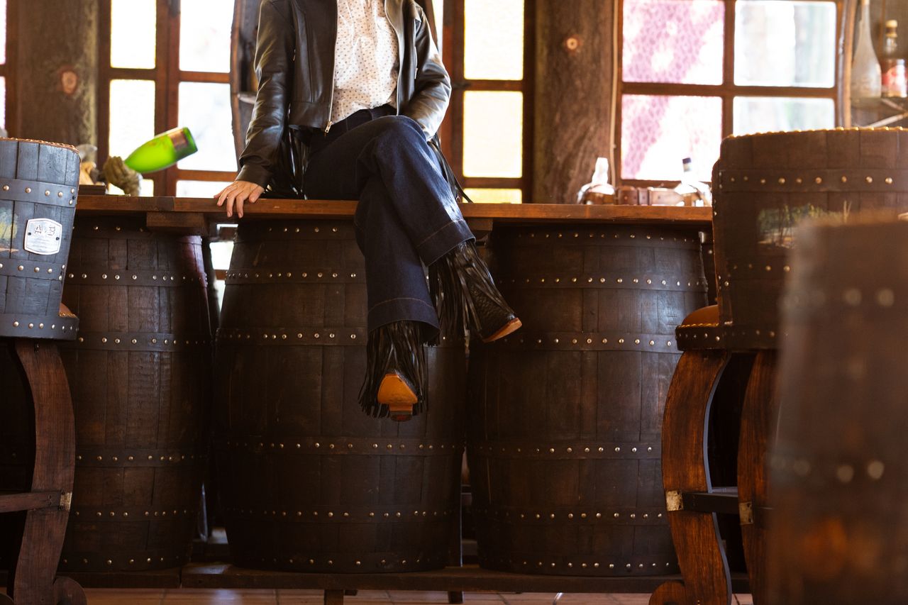 about-img-01 Person in cowboy attire sitting on barrels in a rustic bar, showcasing western style.